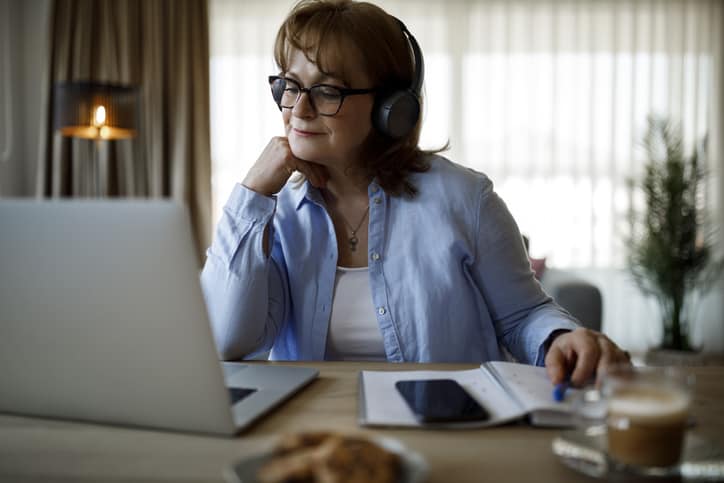 Smiling mature woman with wireless headphones watching webinar on the new undervaluation risk flag and other appraisal topics