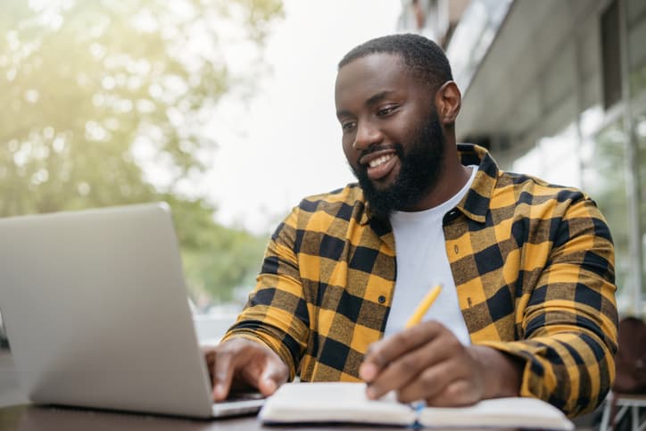 Young handsome African American property appraiser using laptop computer, taking notes, learning online