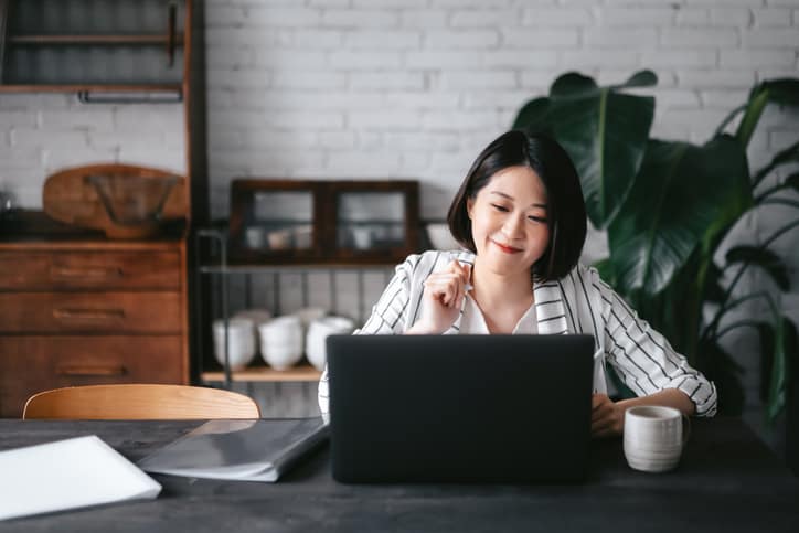 Asian woman attending webinar on laptop, working from home