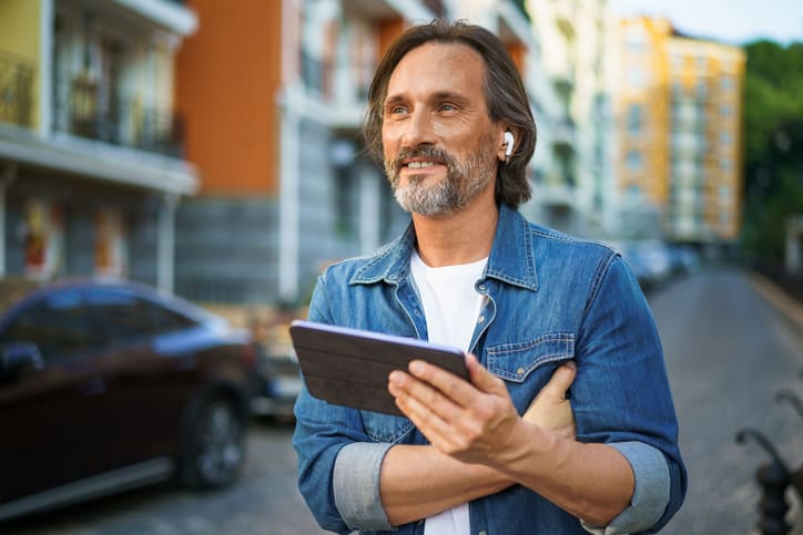 Handsome middle aged real estate appraiser using digital tablet and earphones, professional development on the go