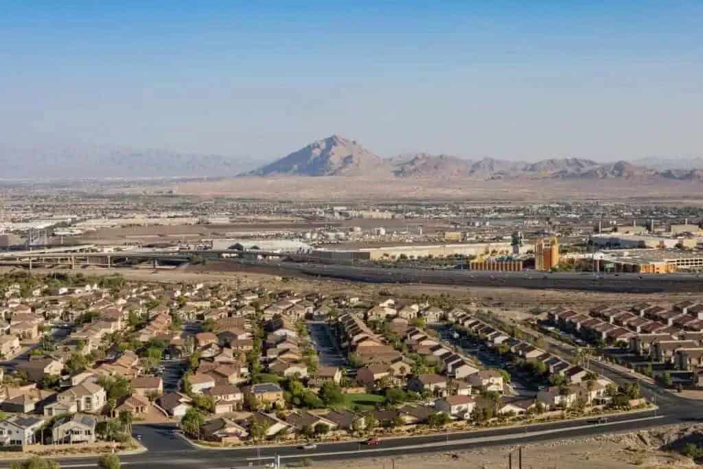 This image shows an aerial view of Henderson, Nevada, with suburban houses, a highway, and mountains in the background.